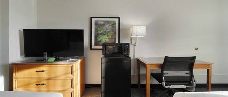 Ein Hotelzimmer mit Fernseher, kleinem Kühlschrank, Schreibtisch und Stuhl sowie einem Bett.
