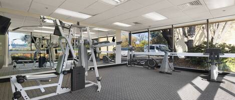 A gym with various exercise equipment, large windows, and a view of the outside.