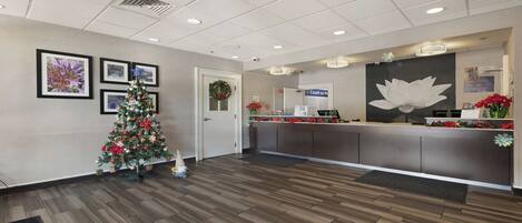 A reception area with a Christmas tree, framed pictures on the wall, a counter with a sign, and a large flower decoration.