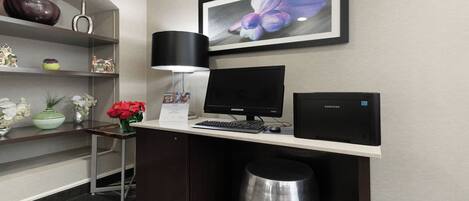 A hotel workspace with a desk, computer, and a framed picture on the wall.