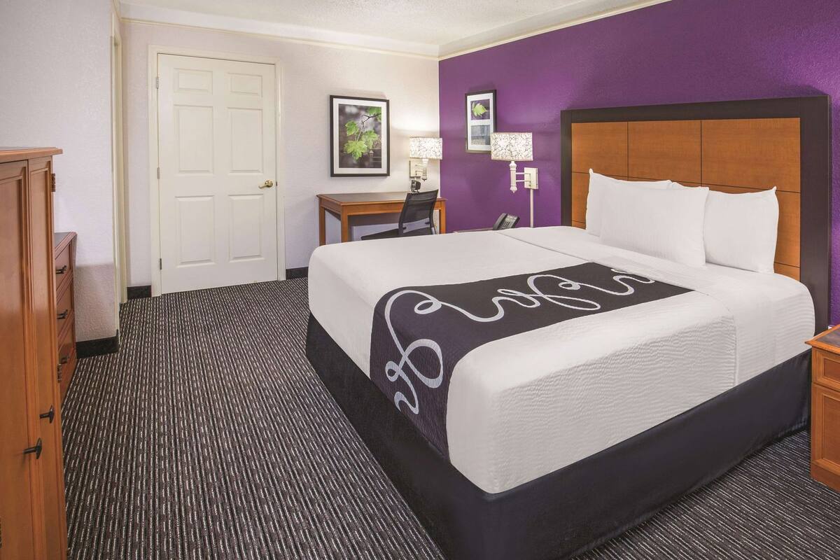Een hotelkamer met een bed, een bureau, een stoel, een lamp en een deur.