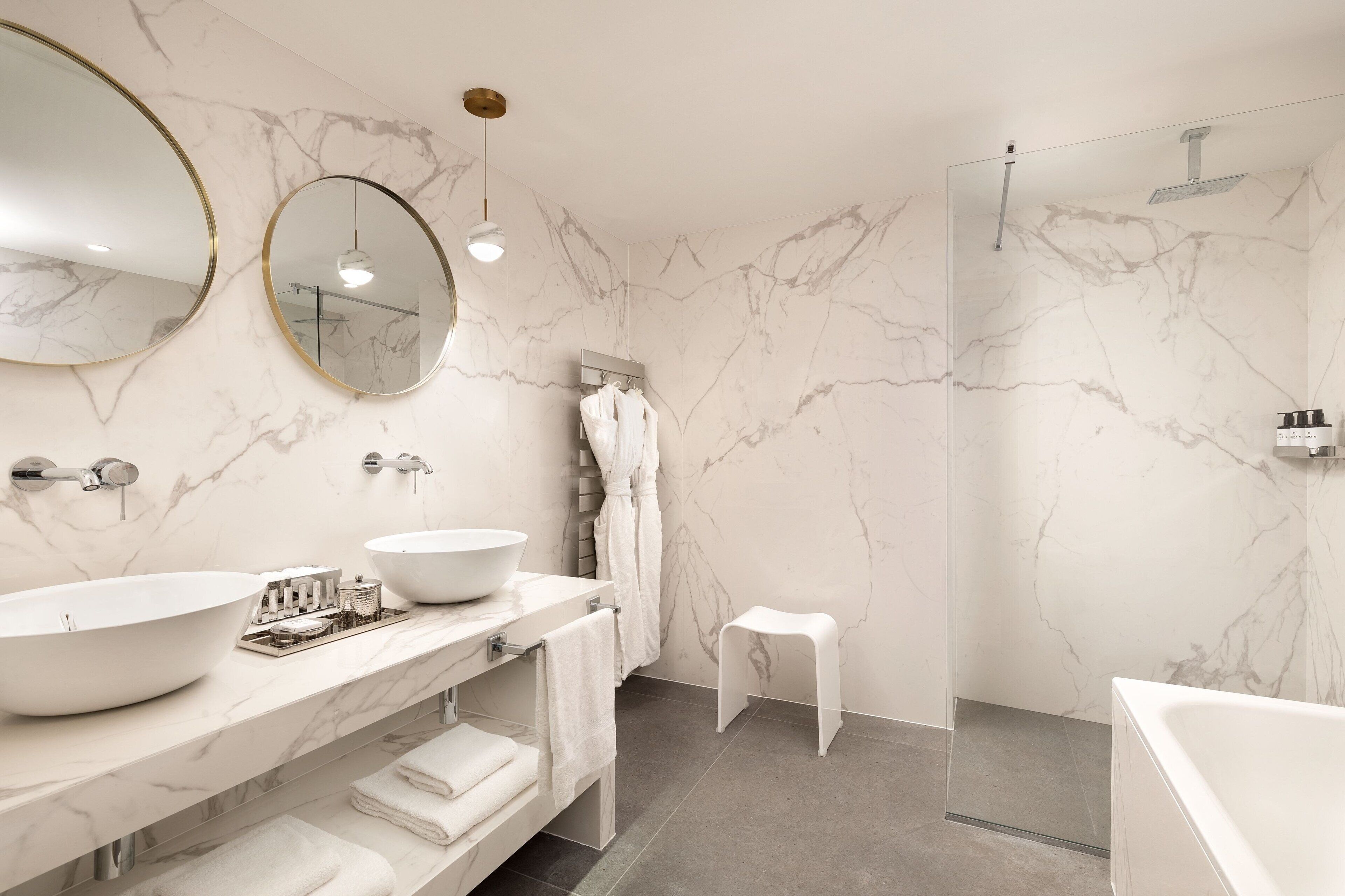 Une salle de bain moderne avec un grand lavabo blanc, deux miroirs, une douche en verre et une baignoire blanche.