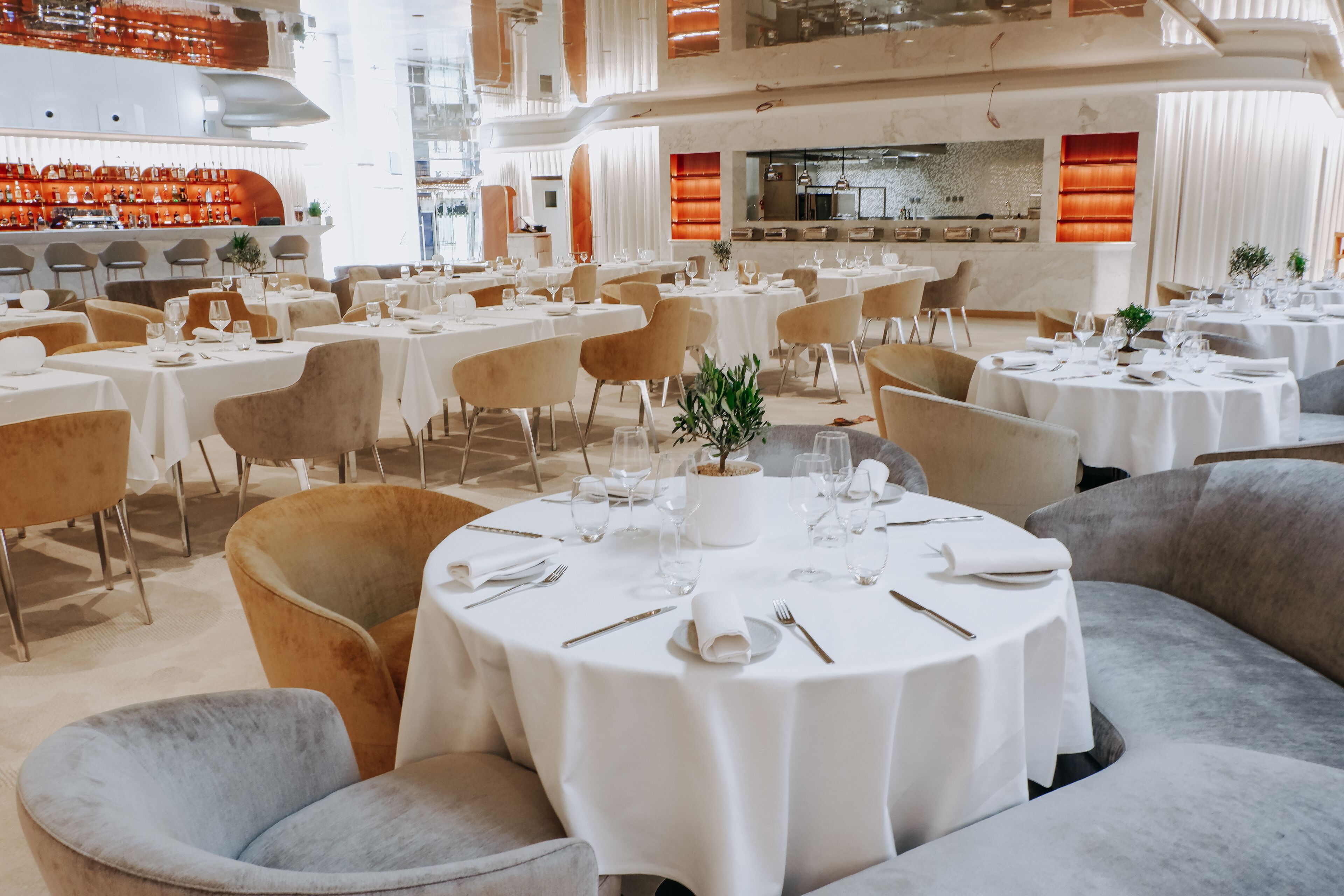 A spacious restaurant with multiple round tables, each set with white tablecloths, plates, and cutlery.