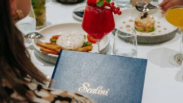 Une table à manger avec différents plats, une boisson rouge aux fruits des bois et un menu intitulé « Scalini ».