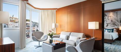 A modern hotel room with a large window, a sofa, a coffee table, and a bed.