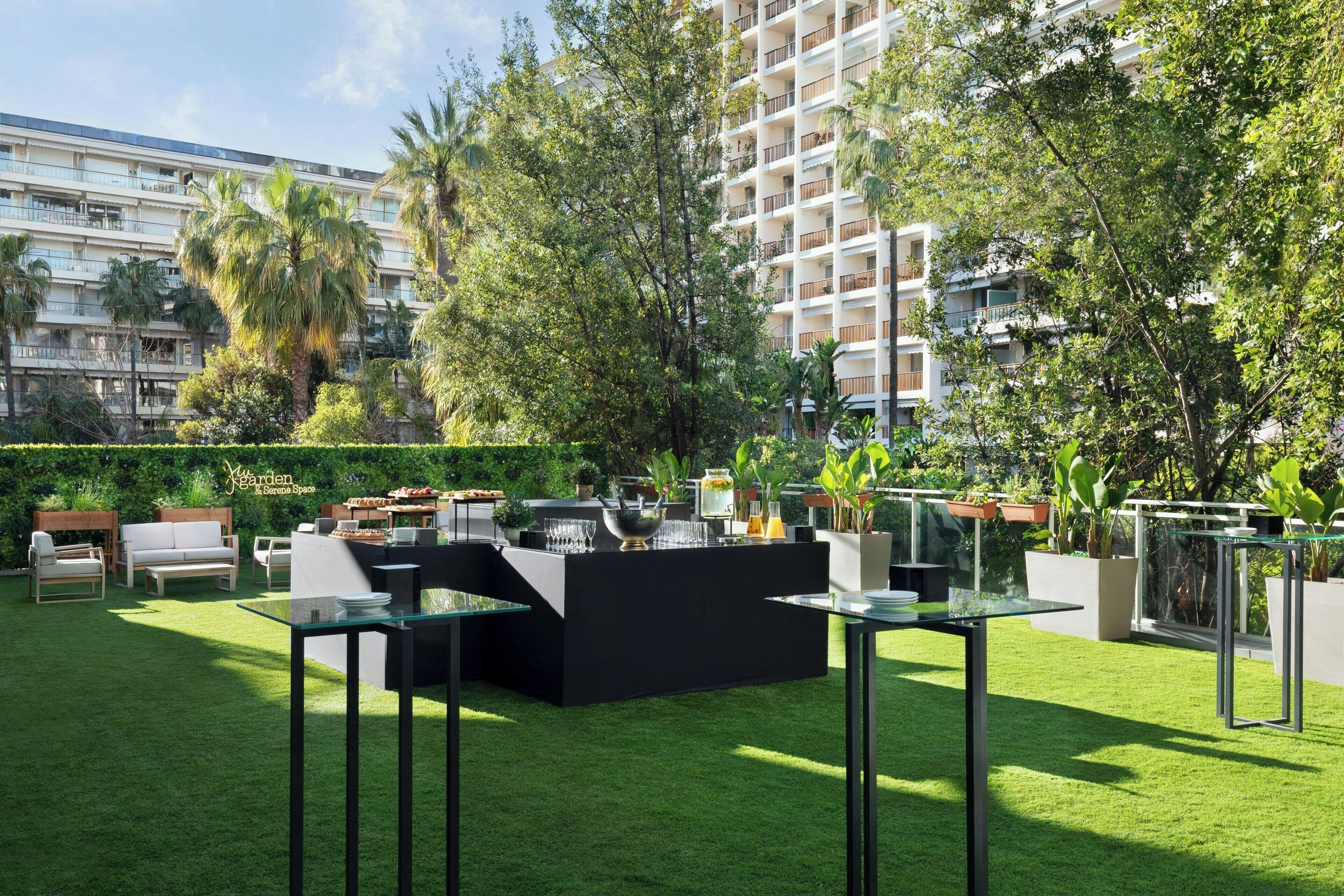 Un espacio exterior cuidado con una distribución moderna de asientos, una zona de bar y abundante vegetación.
