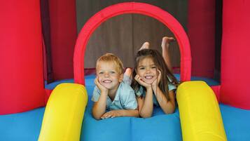 Twee kinderen liggen op een blauw opblaasbed met gele en rode randen, in een rood en zwart opblaasbaar speeltje.