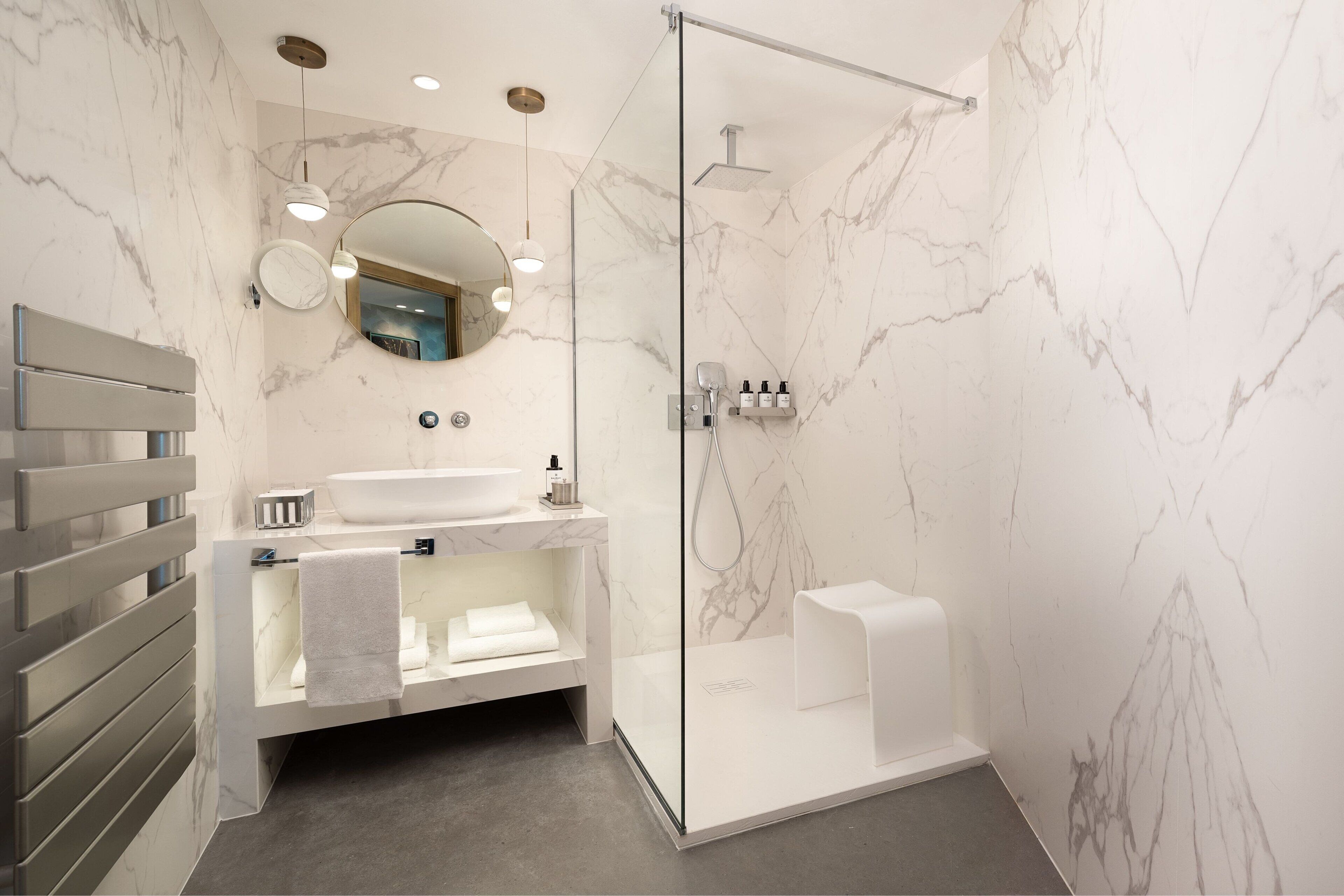 Un baño moderno con pared de mármol, cabina de ducha con vidrio, lavamanos blanco y un perchero para toallas.