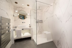 Un baño moderno con pared de mármol, cabina de ducha con vidrio, lavamanos blanco y un perchero para toallas.