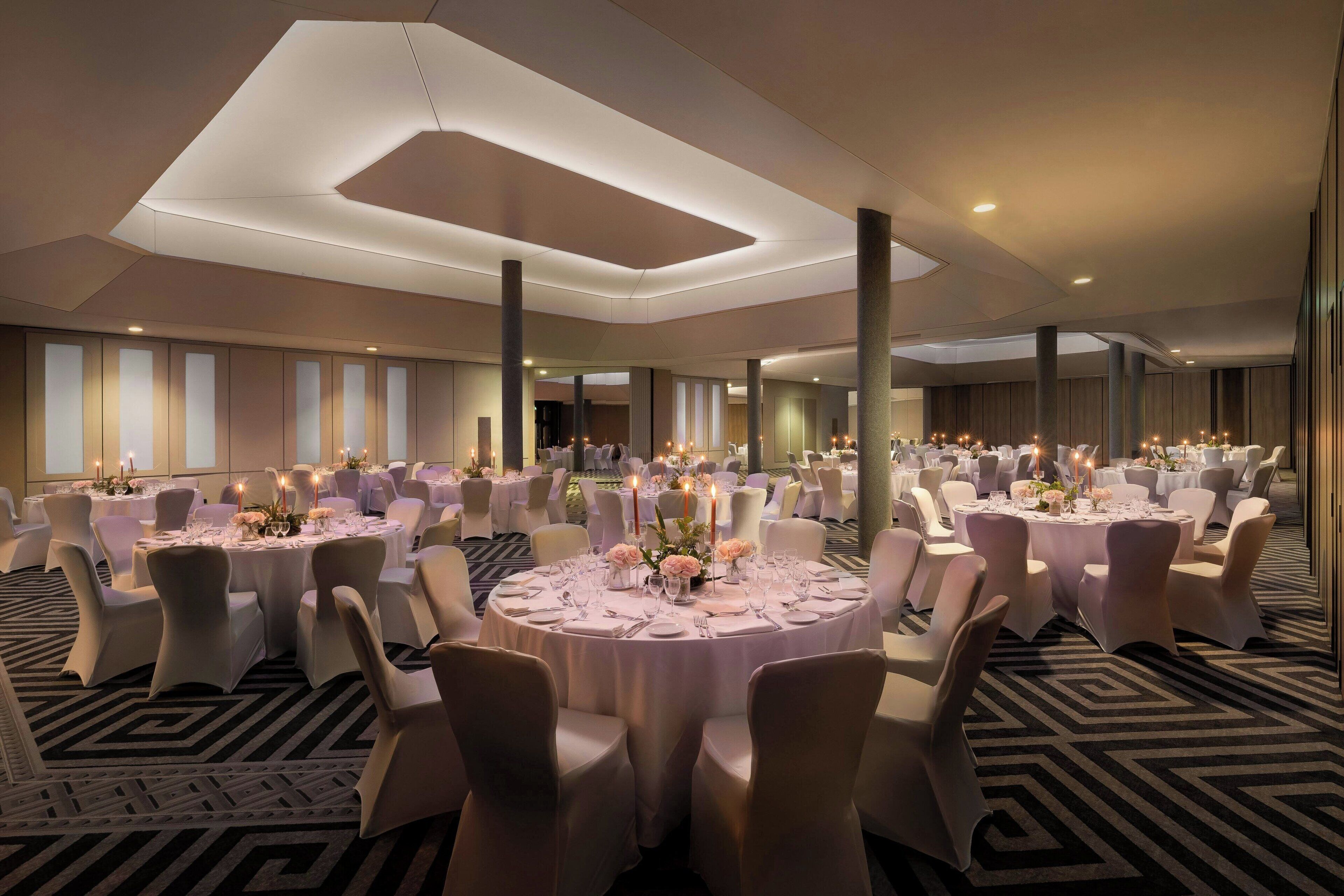 Un amplio salón de banquetes con mesas redondas dispuestas para el servicio de comidas, con manteles blancos y centros de mesa florales.