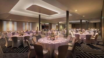 Un amplio salón de banquetes con mesas redondas dispuestas para el servicio de comidas, con manteles blancos y centros de mesa florales.