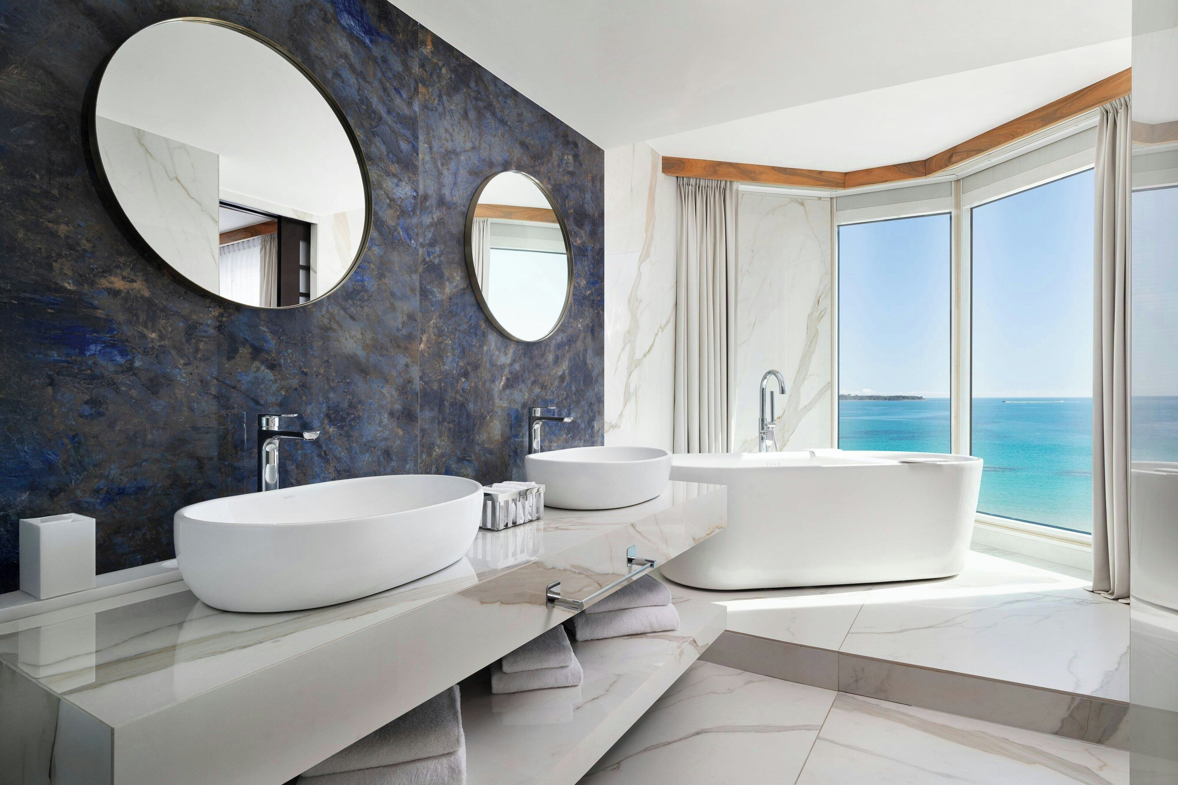 Un bagno moderno con due ampi lavandini bianchi, una vasca da bagno indipendente e un grande specchio.