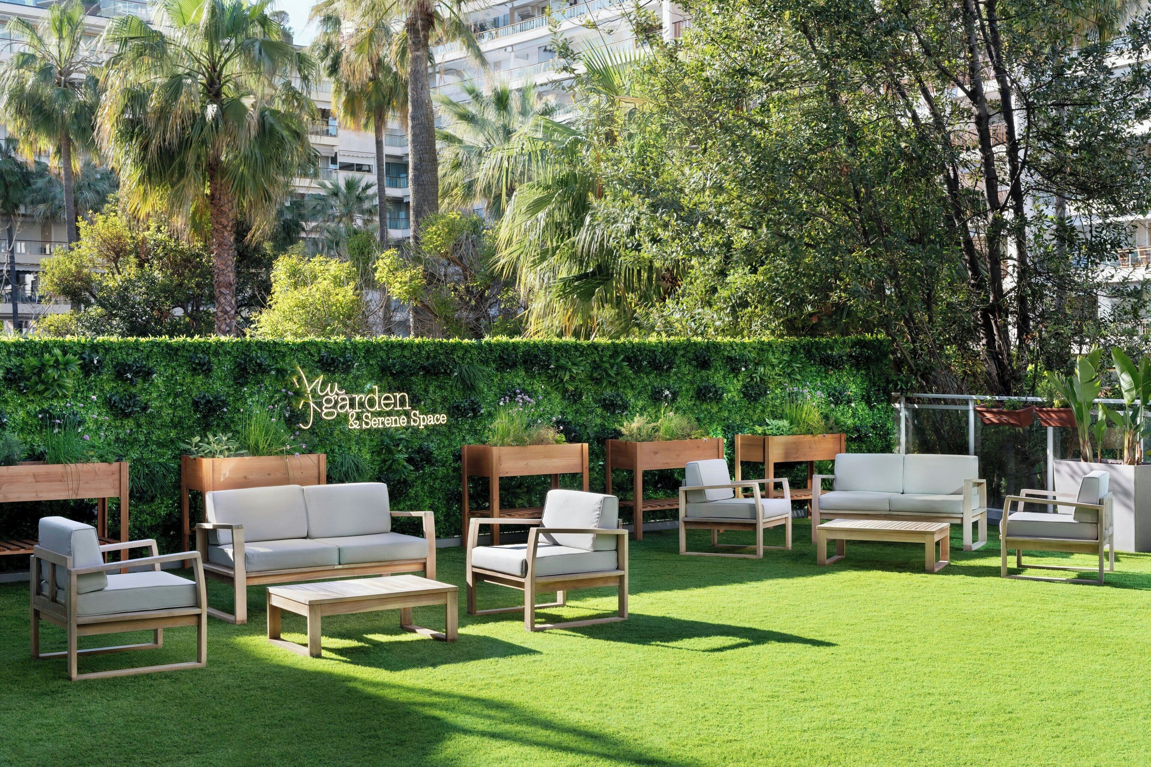 Ein Garten mit Sitzgelegenheiten im Freien, darunter Sofas und Stühle, und ein Hecken im Hintergrund.