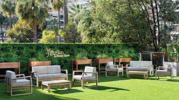 Ein Garten mit Sitzgelegenheiten im Freien, darunter Sofas und Stühle, und ein Hecken im Hintergrund.