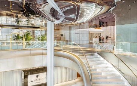 A modern hotel interior with a curved staircase, a visible JW Marriott sign, and a glass railing.
