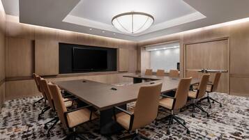 A conference room with a large table, chairs, a flat-screen TV, and a patterned carpet.