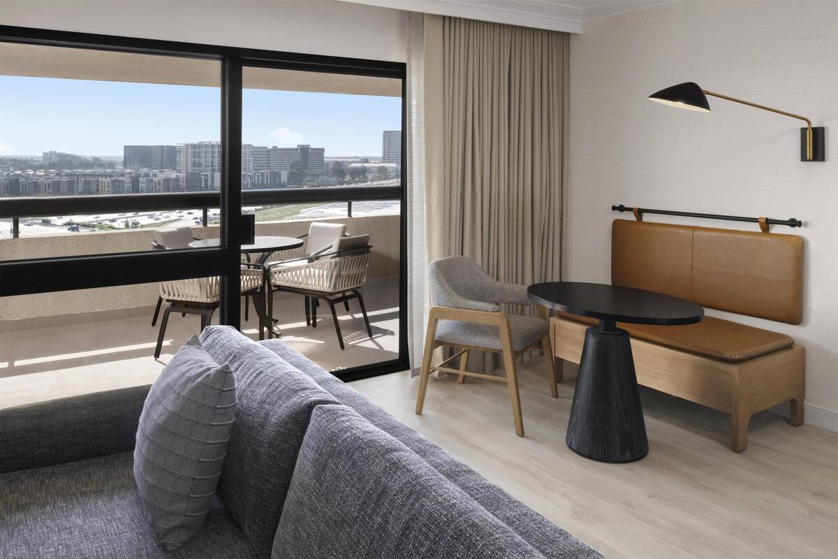 Ein modernes Hotelzimmer mit Balkon, einer Couch, einem Esstisch und einem Stuhl.
