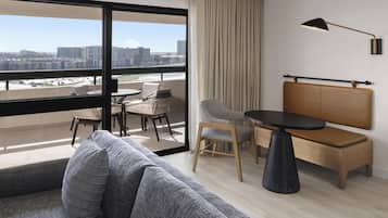 Una habitación de hotel moderna con balcón, sofá, mesa de comedor y una silla.