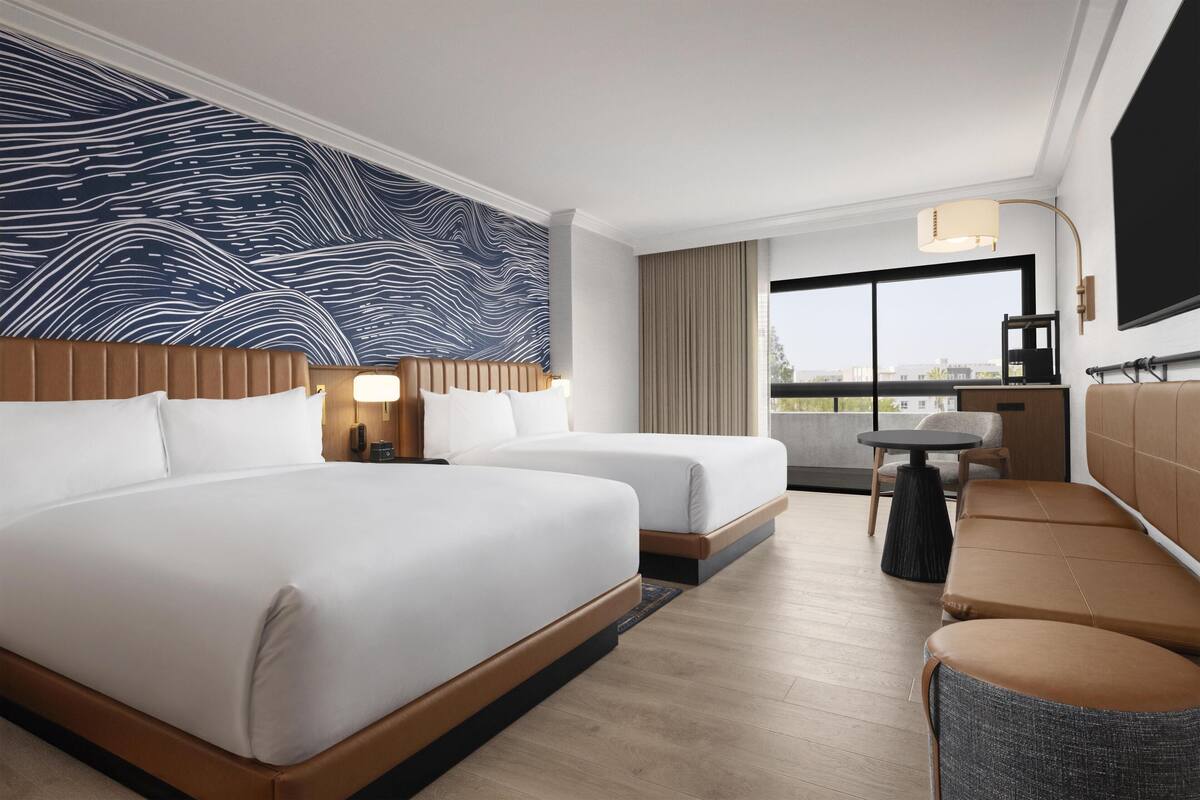 Ein Hotelzimmer mit zwei Betten, einem Sofa, einem kleinen Tisch, einem Fernseher und einem großen Fenster mit Blick.