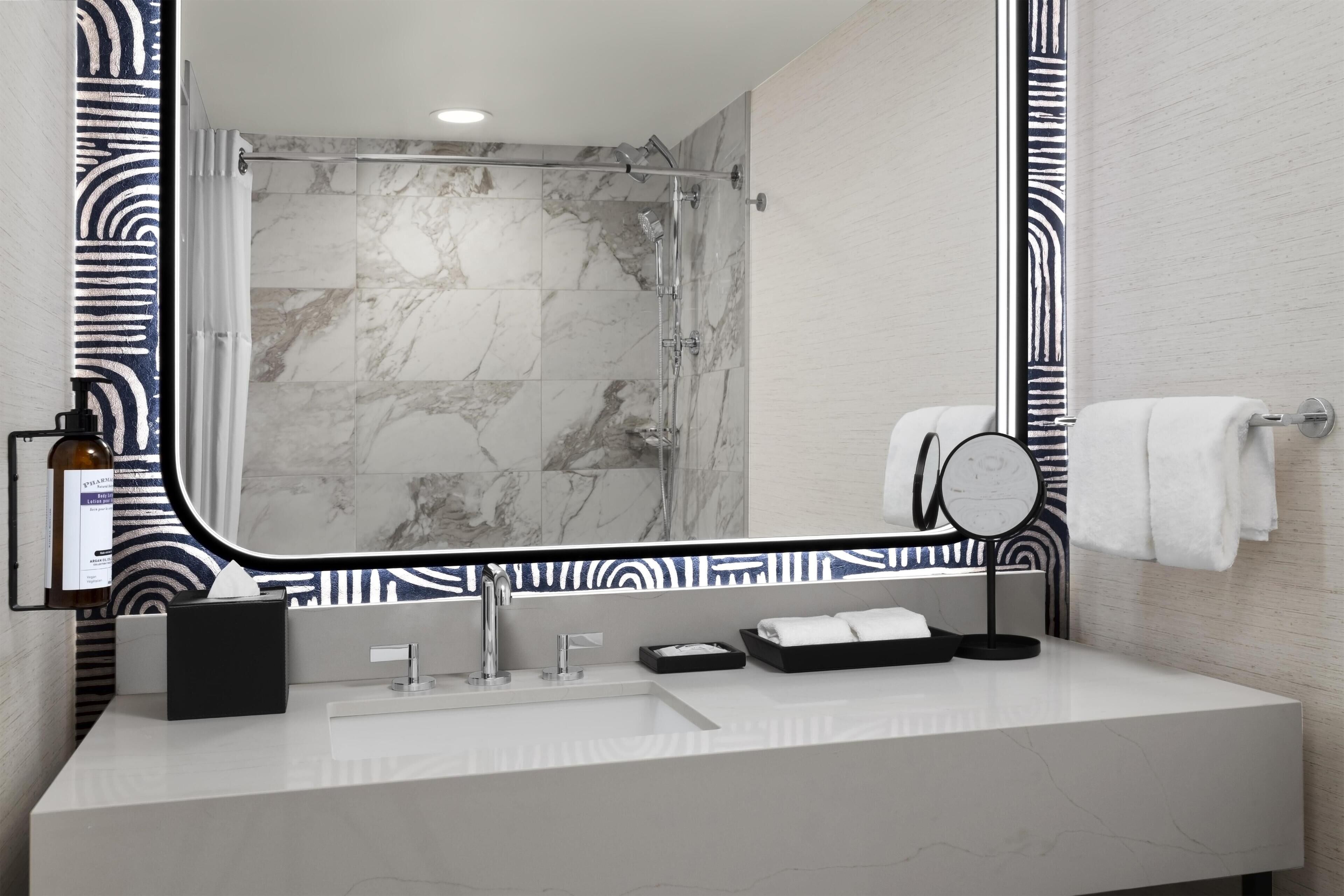 Une salle de bain moderne avec un grand miroir, une douche aux carreaux de marbre, un lavabo blanc et un porte-serviettes.