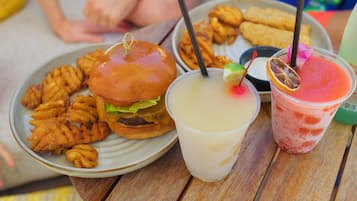 A meal with a burger, fries, and two drinks on a wooden table.