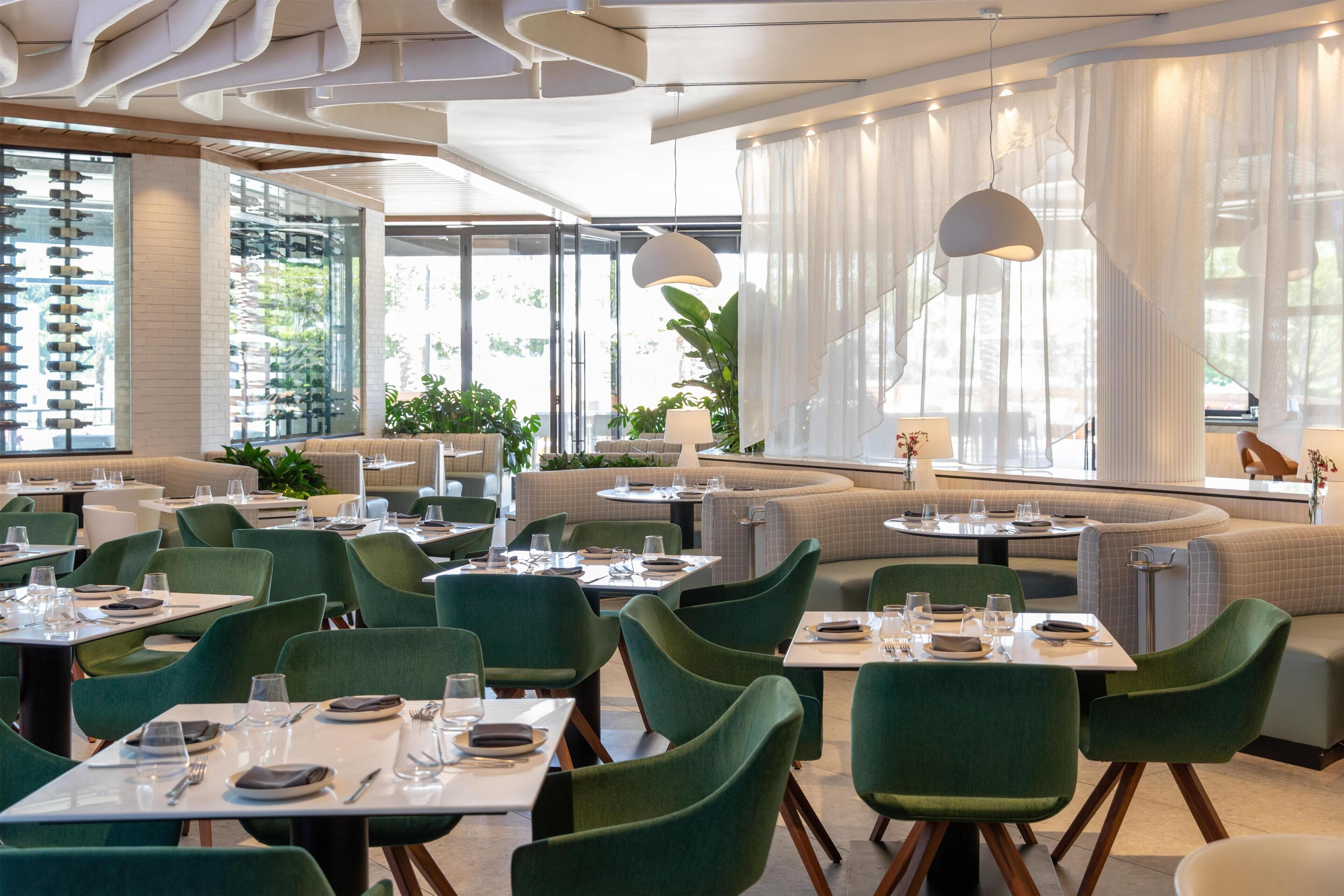 Un restaurant moderne avec des chaises à revêtement vert, des tables rondes et un éclairage combinant des sources naturelles et artificielles.