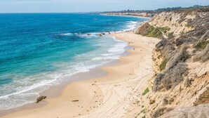 Una playa costera con agua azul cristalina, arena y acantilados rocosos.