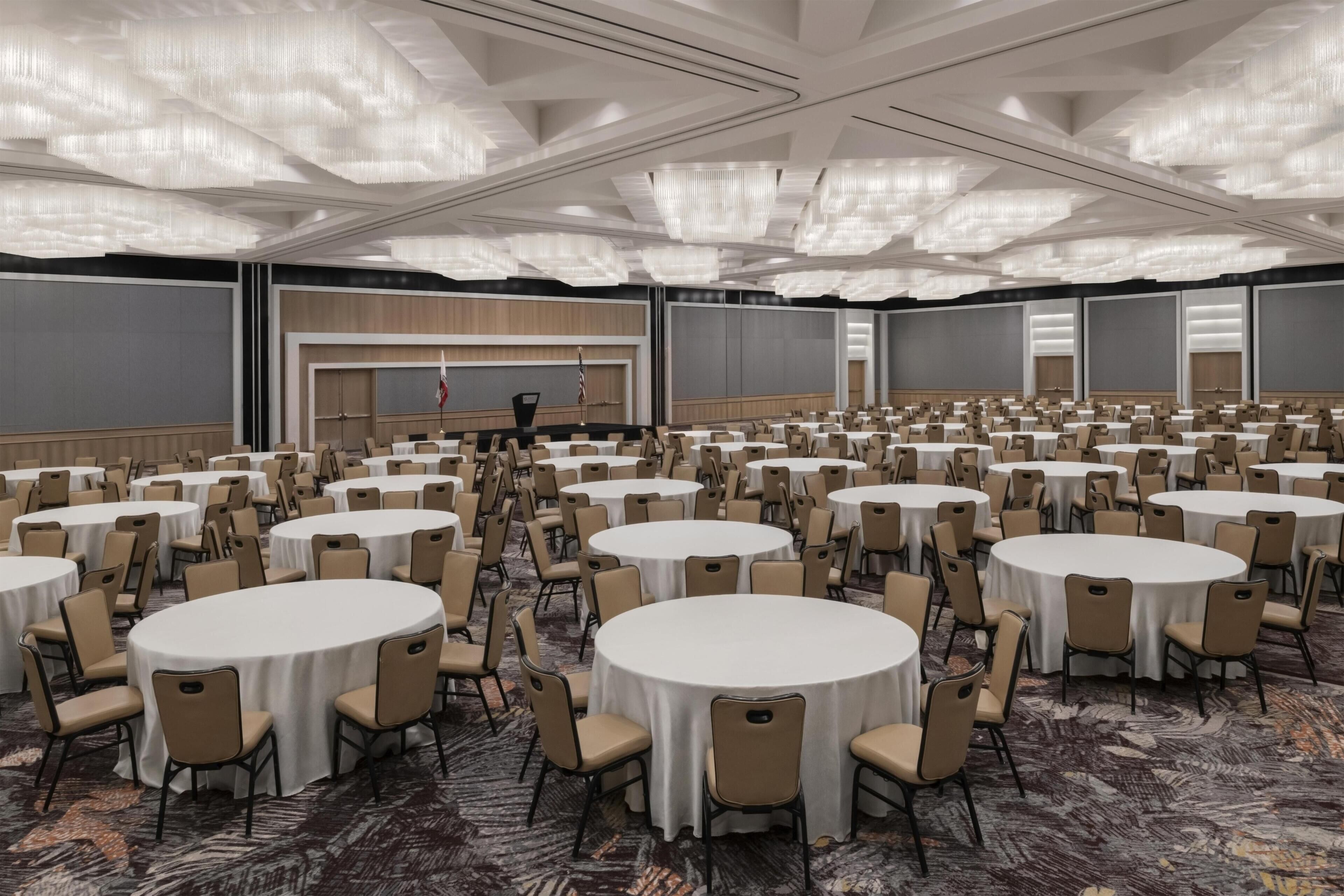 A large conference room with round tables and chairs, a stage with a podium, and a flag.