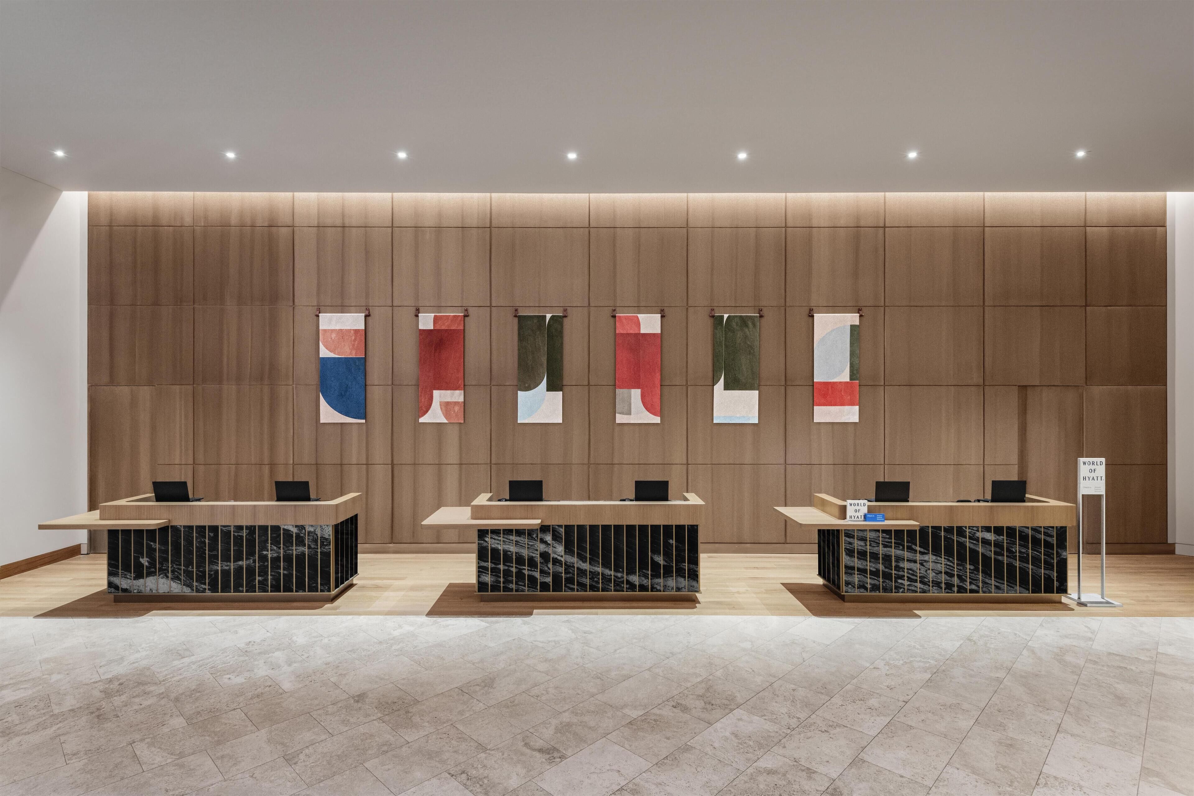 Un espace d’accueil doté de trois comptoirs de réception en marbre, d’un mur en bois avec des panneaux verticaux et d’une enseigne indiquant « Meilleur hôtel du monde ».