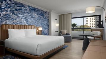 A hotel room with a large bed, a seating area, a balcony with a view, and a modern design.
