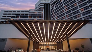 Una entrada de hotel moderna con un vestíbulo cubierto, un mostrador de recepción y zonas de estar.