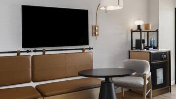 Uma sala de estar moderna com uma televisão de tela plana grande, um sofá, uma mesa redonda, um abajur e um pequeno armário com garrafas.