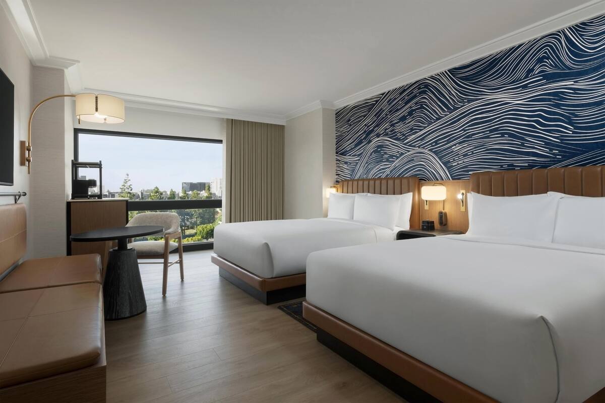 Ein Hotelzimmer mit zwei Betten, einem Schlafsofa, einem kleinen Tisch und Blick auf die Stadt.