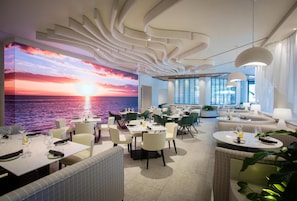 Ein modernes Restaurant mit Sonnenuntergangsmalerei, zeitgenössischen Möbeln und Blick auf das Meer.