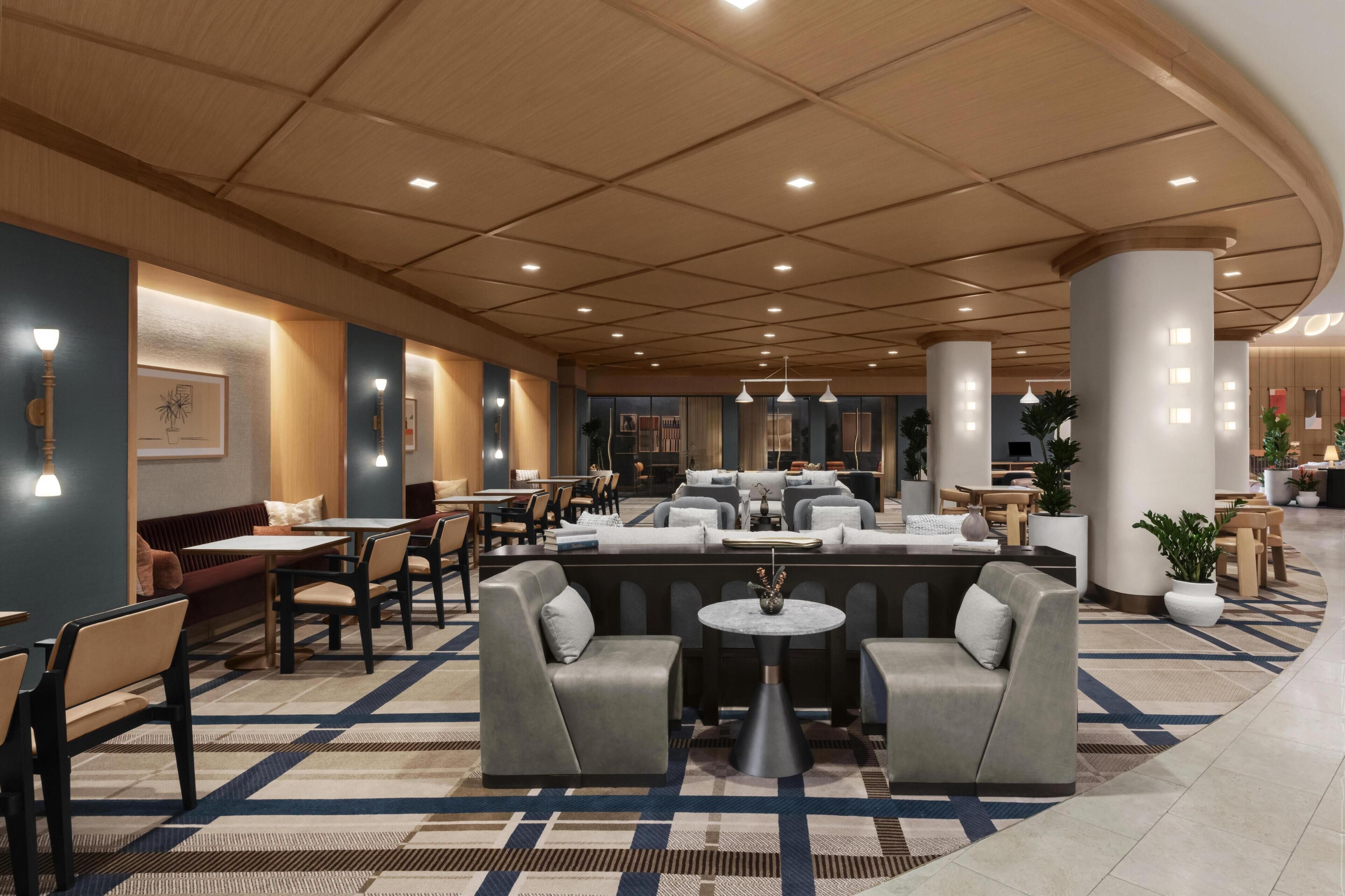A hotel lobby with a central seating area, multiple tables, and a patterned carpet.