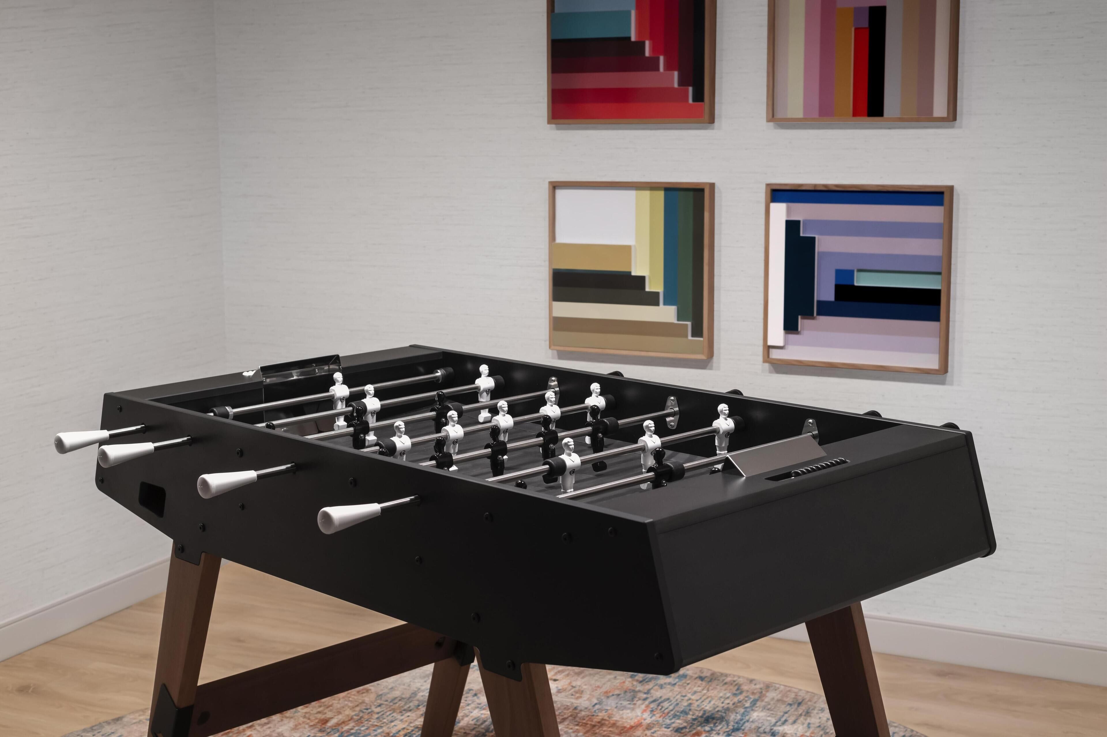 A foosball table in a room with a light-colored wall and abstract art.