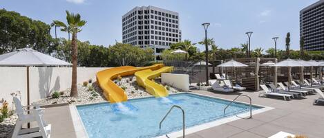 A swimming pool with a slide, lounge chairs, and umbrellas.