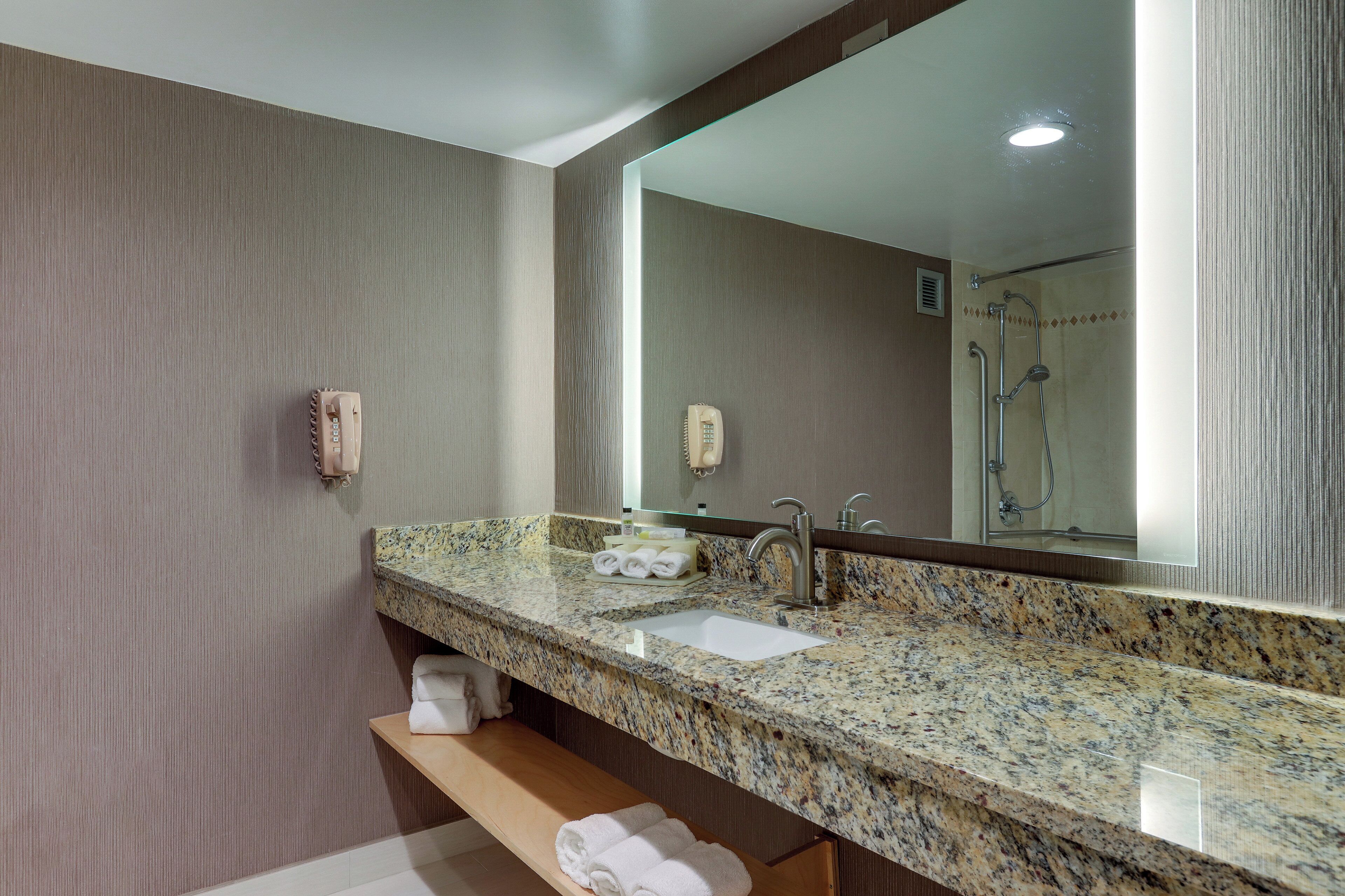 A bathroom with a granite countertop, a sink, a mirror, a towel rack, and a shower area.
