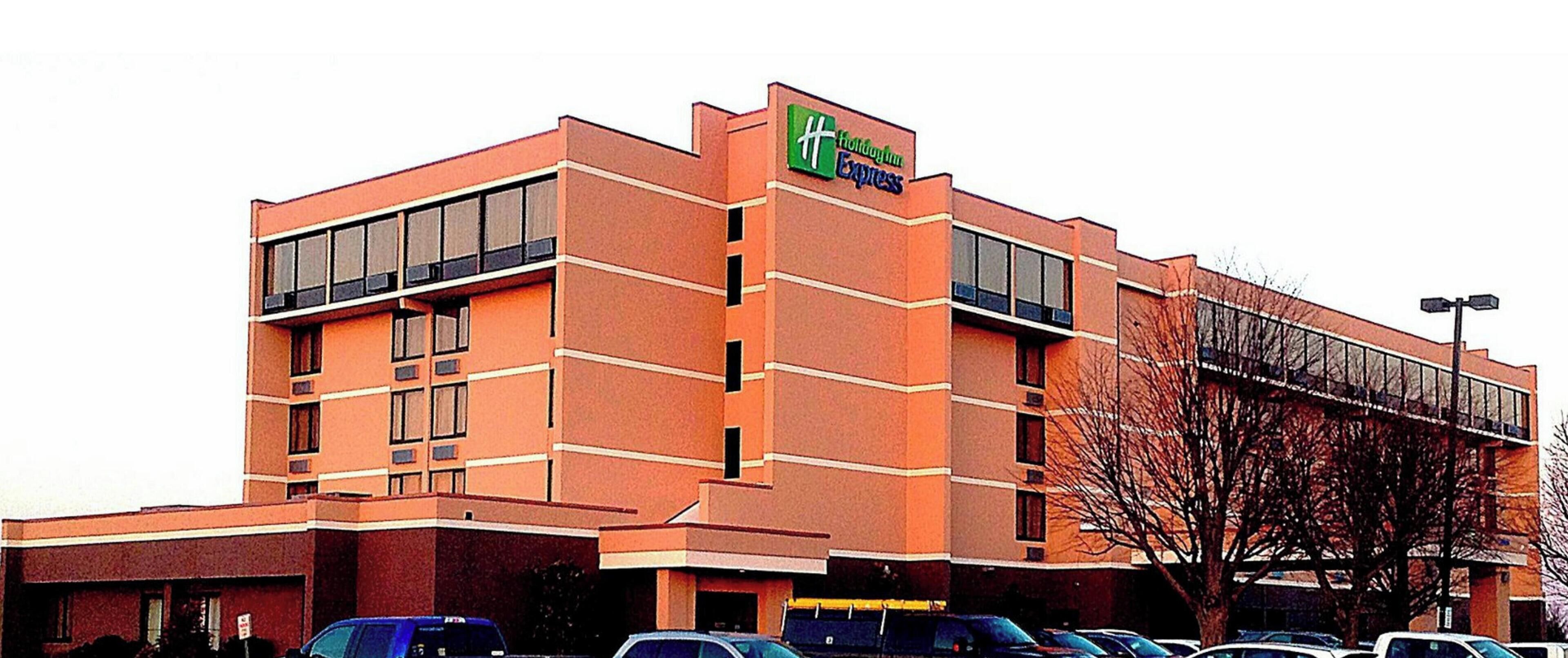 A Holiday Inn Express hotel with a brick facade, large windows, and a parking lot with several cars.