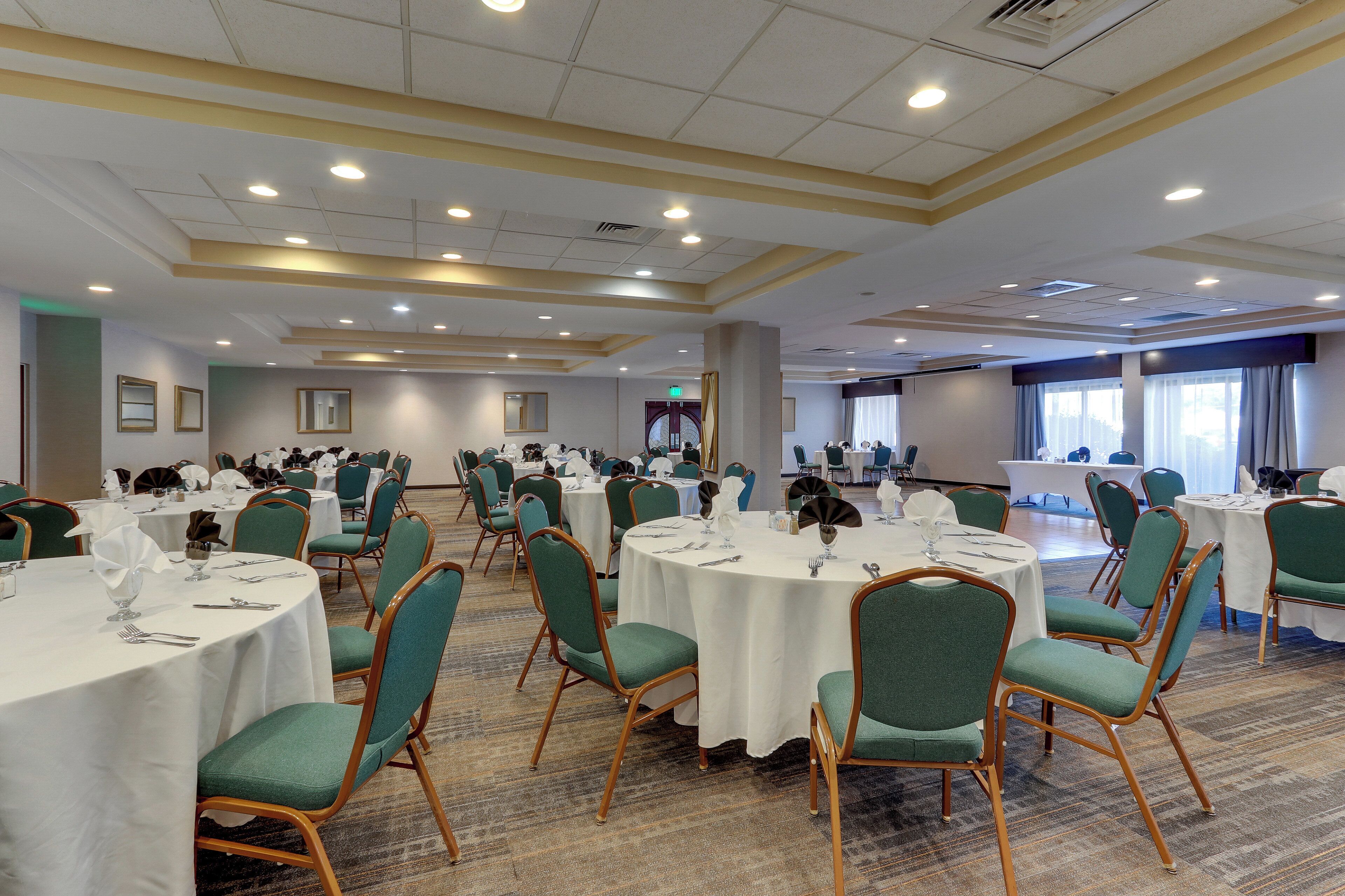 Un salón de conferencias con mesas redondas, sillas verdes y manteles blancos.