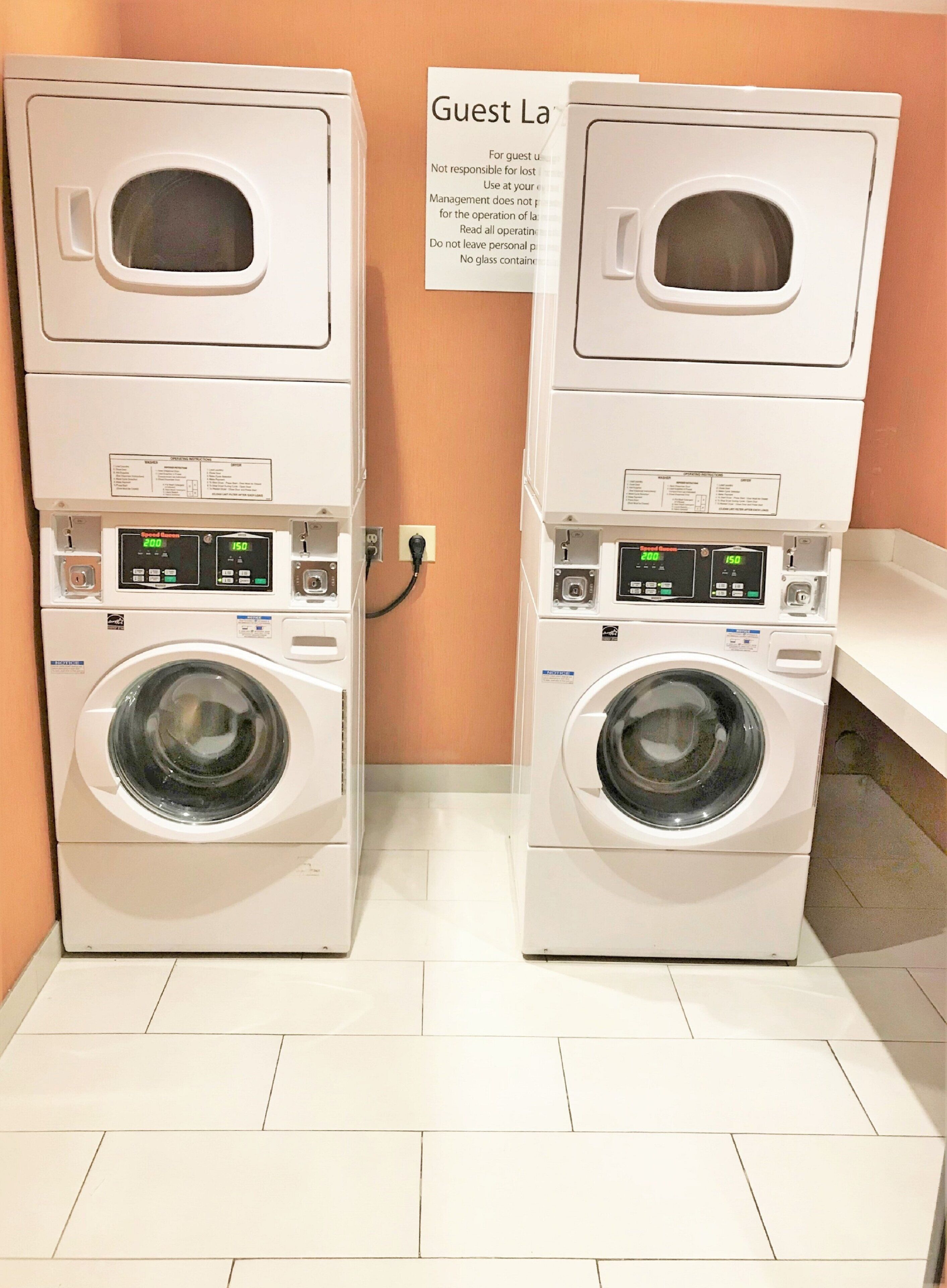 Two stacked front-loading washing machines in a hotel laundry room with a sign above them.