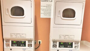 Two stacked front-loading washing machines in a hotel laundry room with a sign above them.