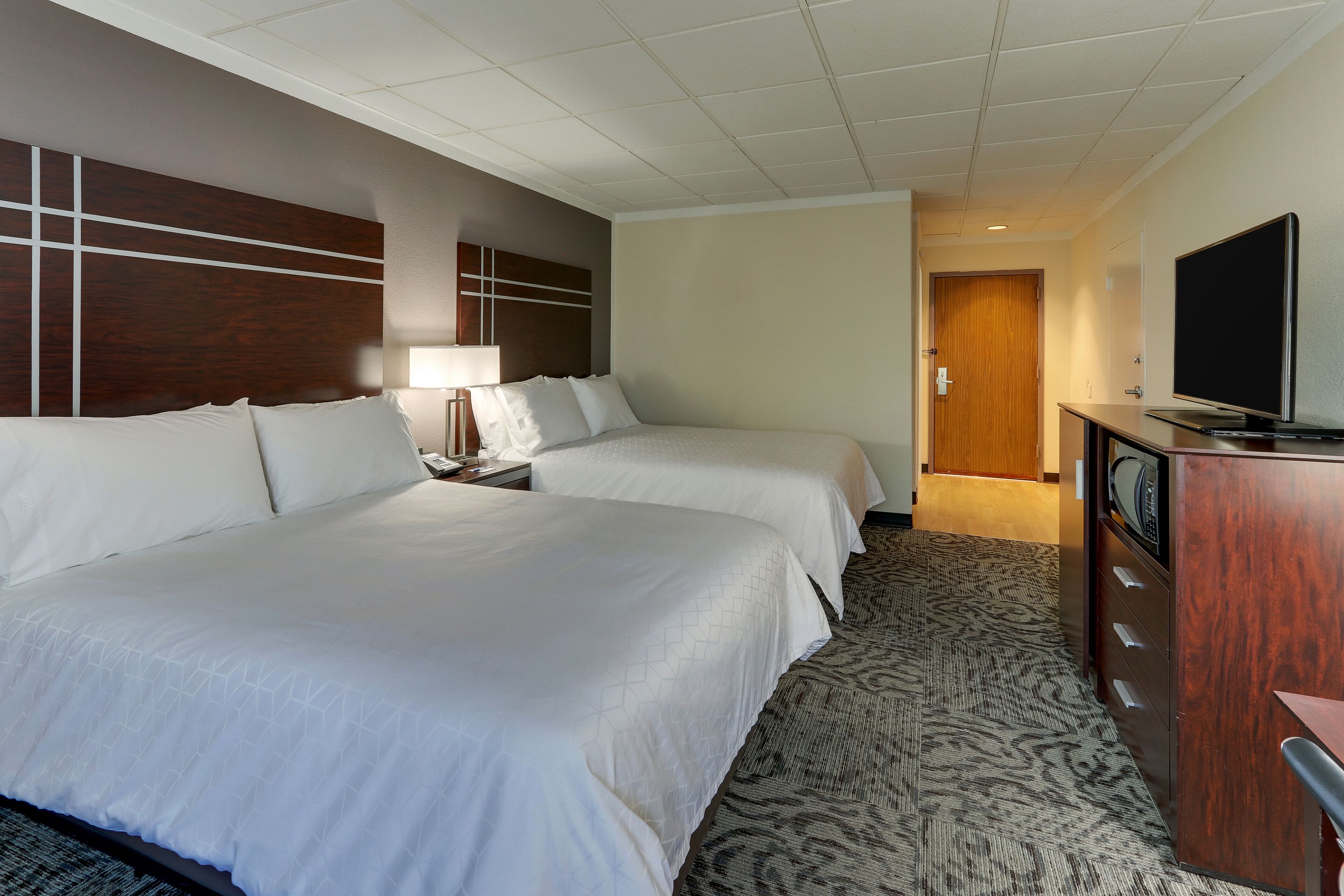 A hotel room with two beds, a desk with a television, and a carpeted floor.