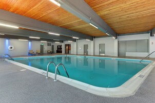 Una piscina interior con techo de madera, zona junto a la piscina despejada y suelo de baldosas.