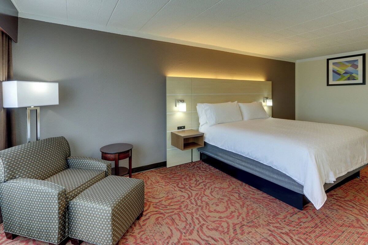 A hotel room with a bed, a sofa, a nightstand, and a lamp.