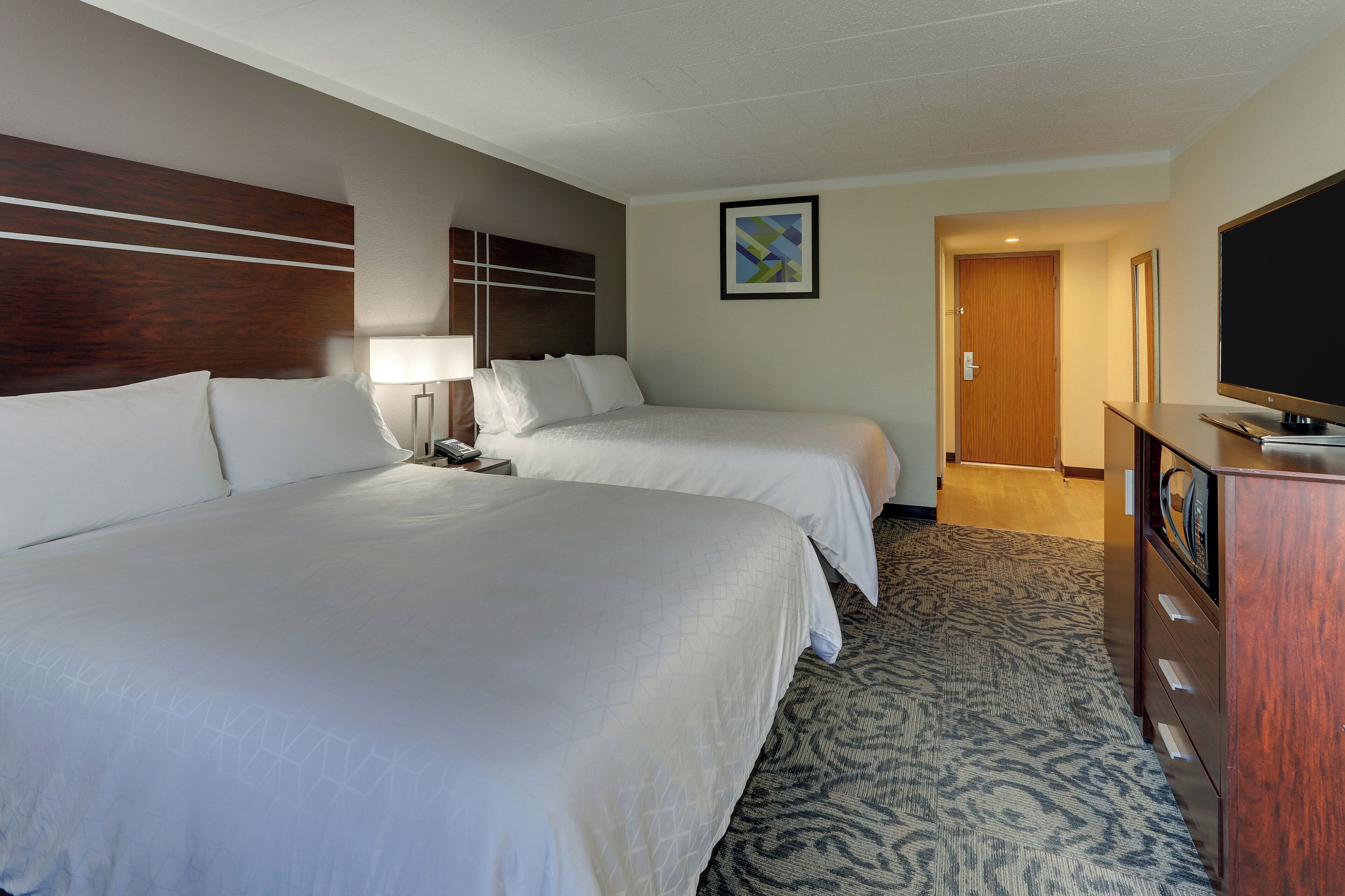 Habitación de hotel con dos camas, televisión, escritorio y piso cubierto de alfombra.
