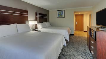 Habitación de hotel con dos camas, televisión, escritorio y piso cubierto de alfombra.
