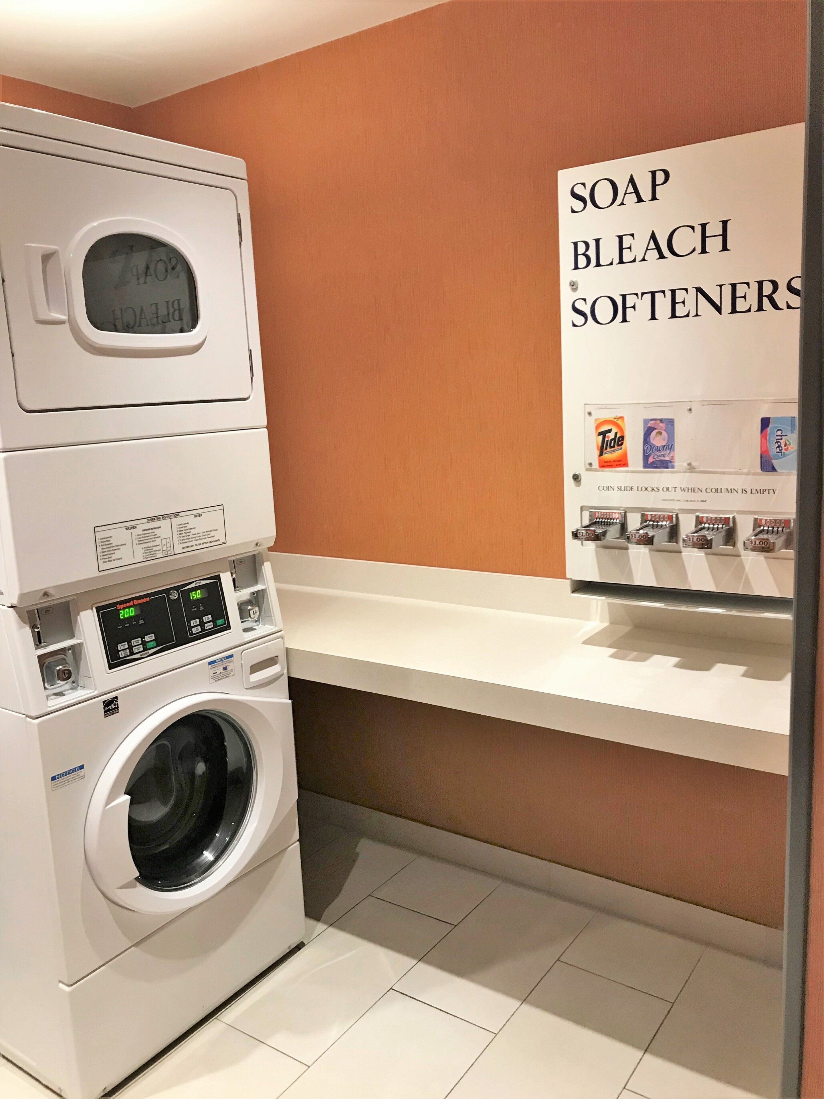 A laundry area with a front-loading washing machine and a shelf with soap, bleach, and softener dispensers.