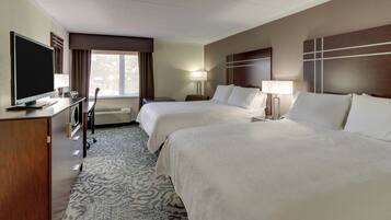 A hotel room with two beds, a television, a desk, and a window with curtains.