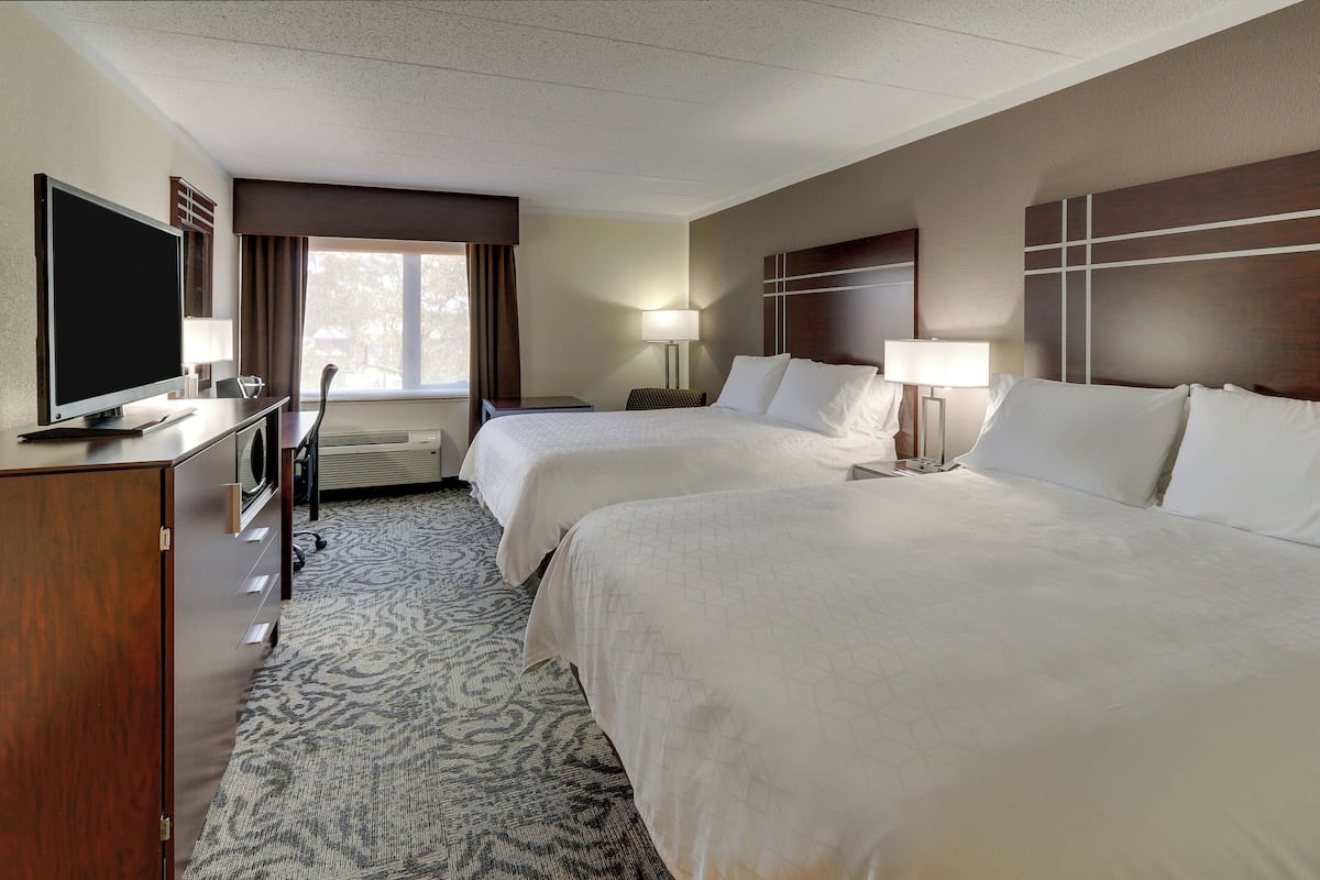 A hotel room with two beds, a television, a desk, and a window with curtains.